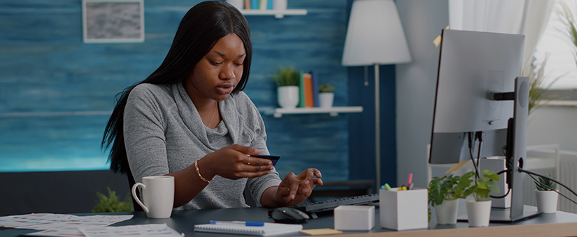 Venda 100% digital: mulher olha para o cartão de crédito enquanto digita ao computador