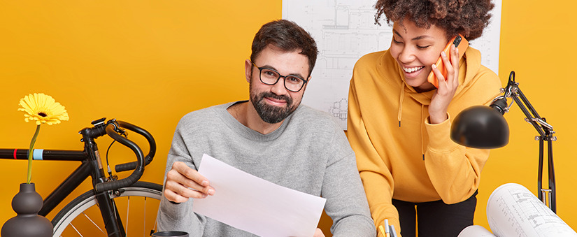 como melhorar o atendimento ao cliente: um homem segura uma folha de papel e olha para frente sorrindo. Ao seu lado uma mulher fala ao celular e sorri