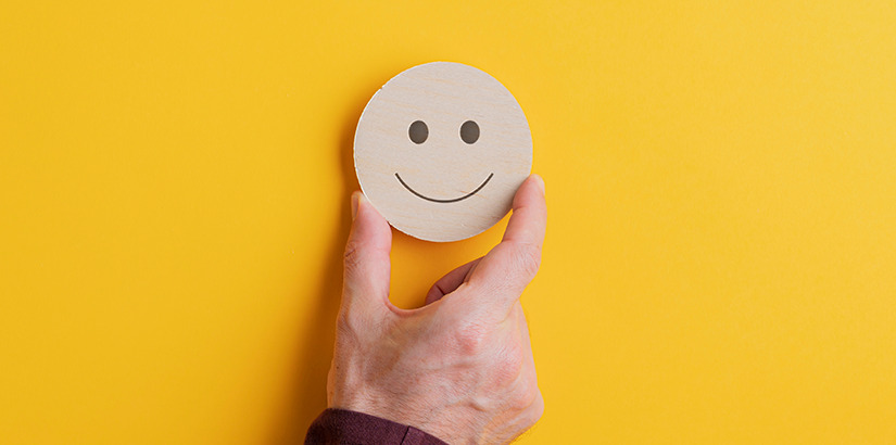 como medir o nível de satisfação do cliente: uma mão segurando um rosto de madeira sorrindo.