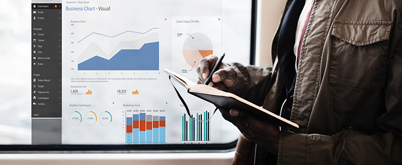 cultura data driven: imagem de uma pessoa escrevendo num caderno e, atrás, um dashboard com vários gráficos.