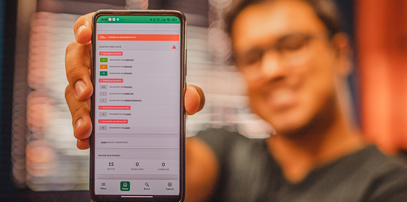 CRM imobiliário: close na mão de uma pessoa segurando um celular com o aplicativo do CV em destaque.