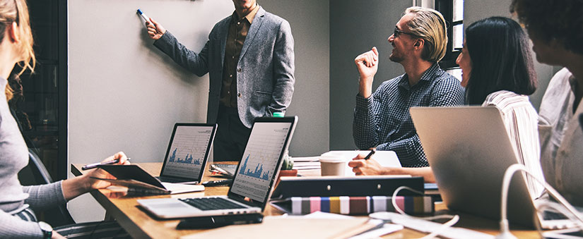 gestão com CRM: imagem de pessoas numa mesa de reunião com notebooks e papeis.