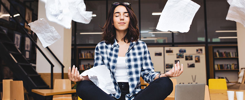 Inteligência emocional: imagem de uma mulher em posição de meditação com alguns papeis voando em volta.