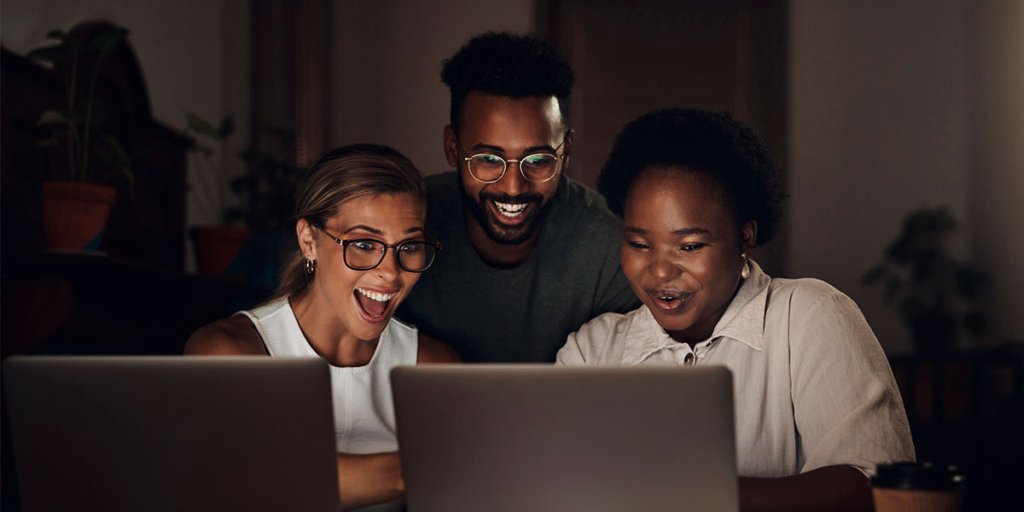 Serasa API: trêspessoas olhando para um notebook com expressões de surpresa e felicidade.