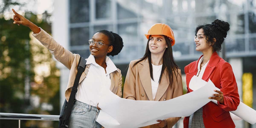 Técnico em edificações: imagem de três mulheres segurando papeis grandes e apontando para o alto.