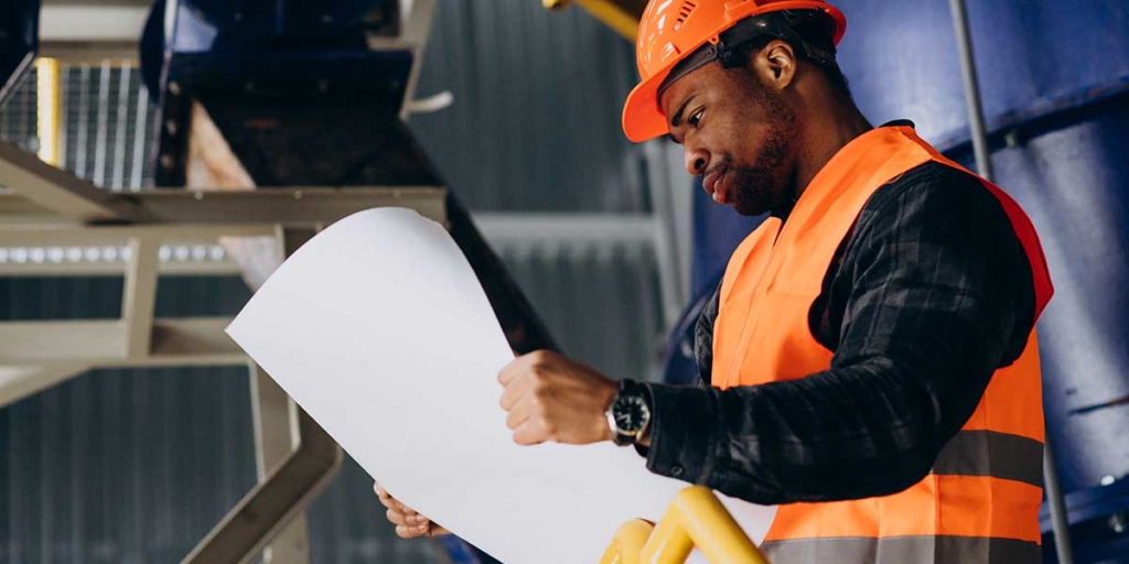 Técnico em edificações: homem com roupas de proteção olhando um papel grande.