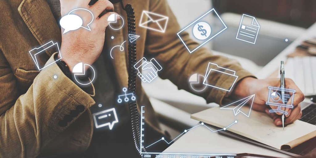 tecnologia persuasiva: cole nas mãos de uma pessoa escrevendo num papel numa mesa cheia de papeis. À frente alguns ícones de balões de fala, aperto de mão, gráficos e cédula de dinheiro.