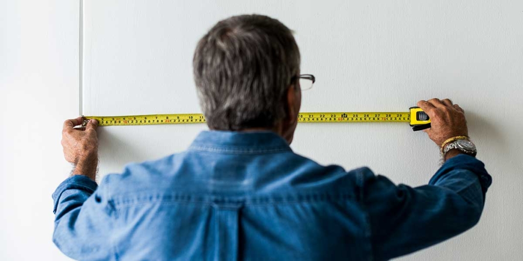 metro quadrado: homem de costas medindo uma parede.