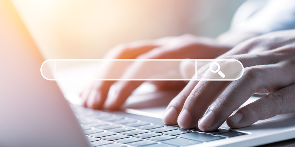 Site de imóveis: close em mãos num teclado de notebook. À frente uma caixa de busca.