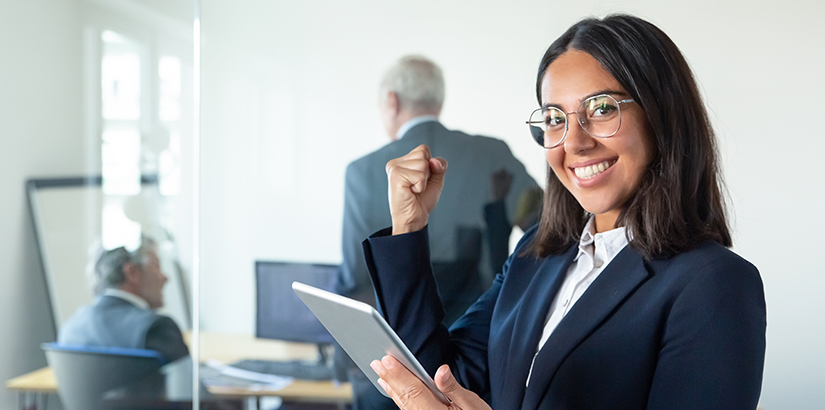 CRM tem as mesmas características e funções que o ERP: mulher de terno, segurando um tablet e olhando para a câmera com expressão de felicidade.