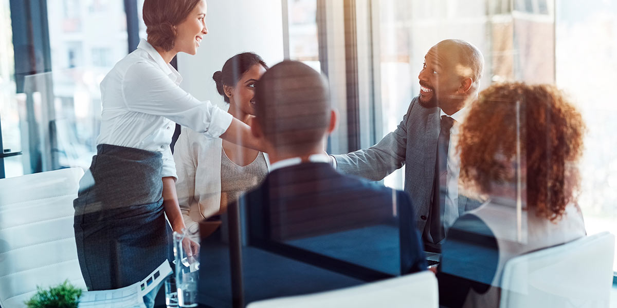 Onboarding de clientes: grupo de pessoas em círculo, numa sala de reunião. No meio, duas delas apertam as mãos.