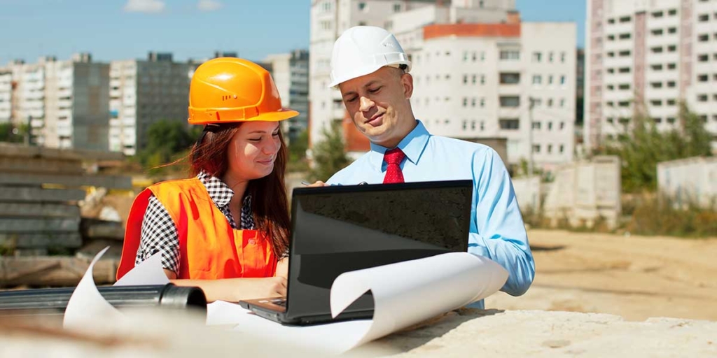 Dia do Engenheiro Civil: imagem de um homem e uma mulher num canteiro de obras, olhando para um notebook.