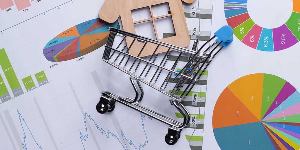 O que é INCC: imagem de um carrinho de compras em miniatura em cima de alguns papeis com gráficos coloridos