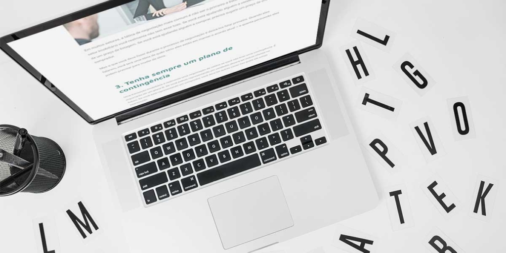 Palavras que despertam interesse: imagem de uma mesa vista de cima com um notebook e algumas letras espalhadas pela mesa.