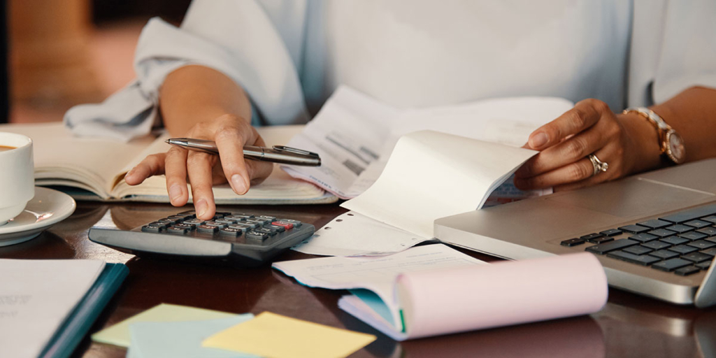 Taxa de ocupação e coeficiente de aproveitamento: imagem das mãos de uma pessoa numa mesa segurando alguns papeis com uma das mãos e, com a outra, usando uma calculadora.
