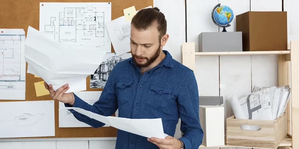 Manual do Proprietário: imagem de um homem num escritório segurando alguns papeis. Ao fundo vemos um mural com algumas plantas de imóveis.