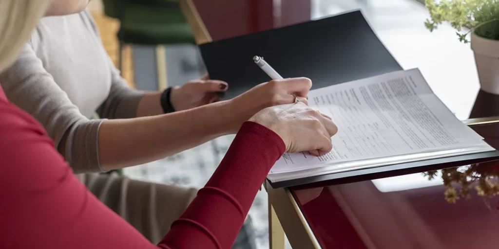 Manual do Proprietário: close nas mãos de duas pessoas assinando alguns papeis.