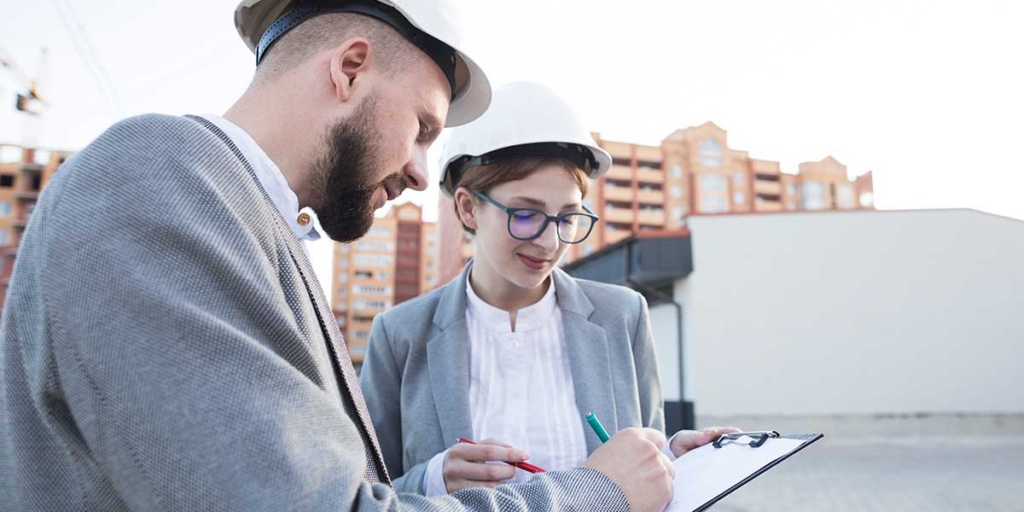 Relatório de visita técnica: duas pessoas num canteiro de obras, olhando para um papel.