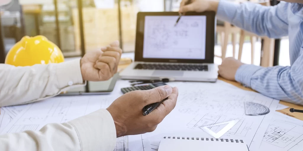 NIRF: imagem de uma mesa com muitos papeis e um notebook. De um lado vemos as mãos de uma pessoa apontando para o notebook, do outro, mãos de outra pessoa.
