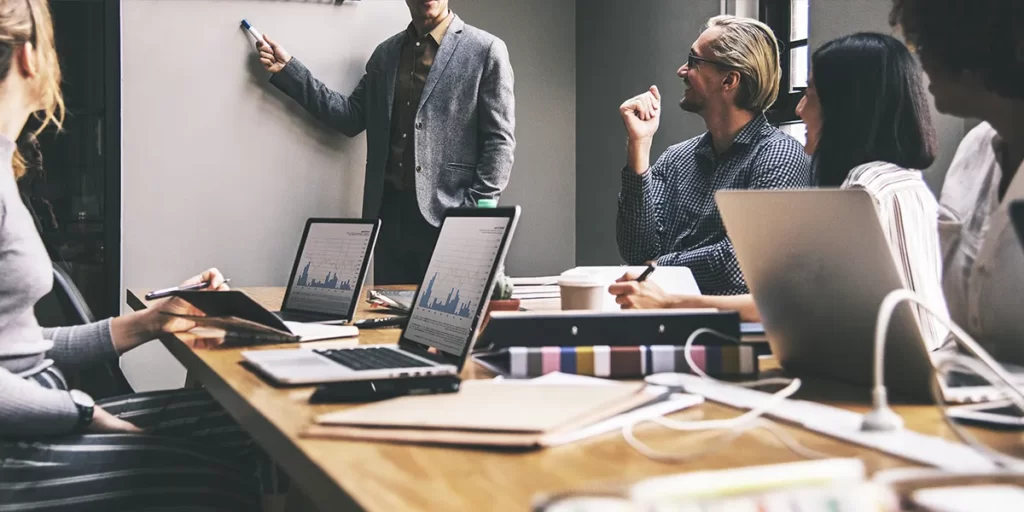 Negócios lucrativos na construção civil: imagem de uma sala de reunião com algumas pessoas em volta da mesa com notebooks e gráficos na tela.