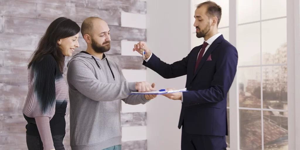 Ficha de visita de Imóvel: imagem de um homem, que veste um terno, entregando uma chave para um casal.