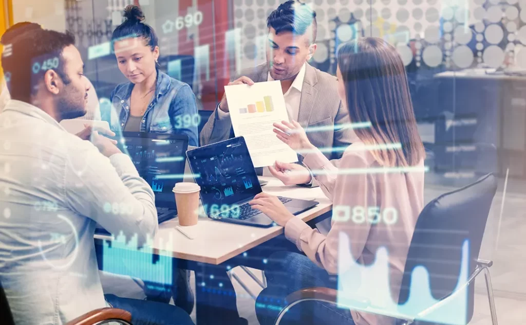 Como prospectar mais clientes: imagem de algumas pessoas em volta de uma  mesa de reunião segurando papeis com gráficos e notebooks.