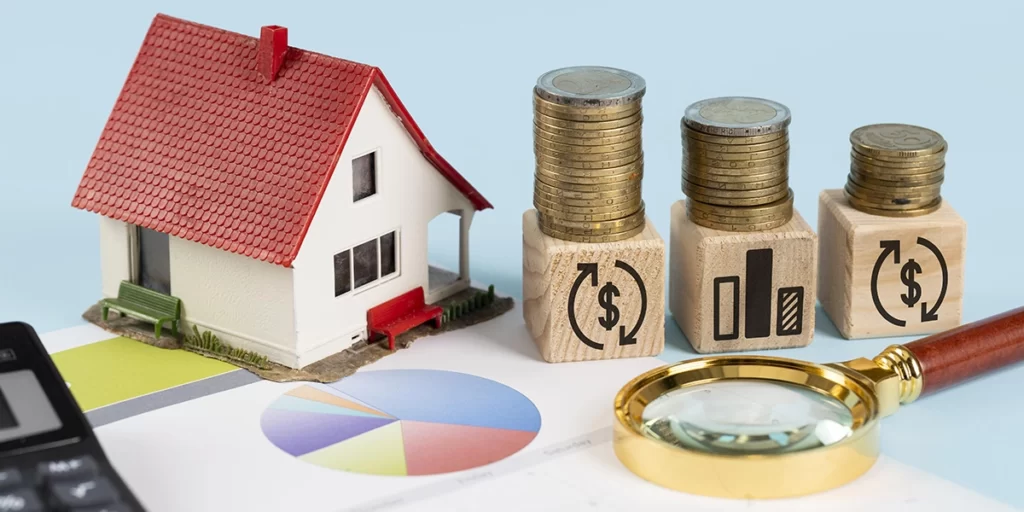 Índice Imobiliário: A imagem mostra uma representação financeira. Há uma casa de brinquedo com uma telhas vermelhas, um banco de moedas de diferentes tipos e valores, um calendário de mês, um contador de dinheiro, um estoque de moedas e um olho de peneira. Tudo isso está sobre um papel com um gráfico de rosa de ponto e um contador de dinheiro.