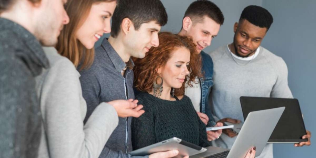 tecnologia no mercado imobiliário: grupo de seis pessoas segurando tablets e notebooks. Todos olham para a tela do notebook de uma das mulheres.