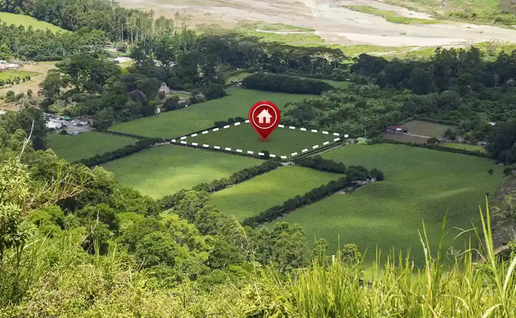 Venda de Loteamento: A imagem mostra uma vista aérea de uma área rural com campos de grama verde e áreas de floresta. Há uma marcação com um ponto vermelho e um símbolo de casa, indicando um local específico dentro do campo. A área marcada parece ser um terreno a ser vendido ou alugado, conforme sugerido pelo símbolo de casa e o texto "Casa". Ao redor do terreno marcado, há linhas que parecem delimitar o terreno disponível. Ao fundo, há outros terrenos e áreas de vegetação, sugerindo que esta área é parte de uma comunidade rural ou uma área agrícola.