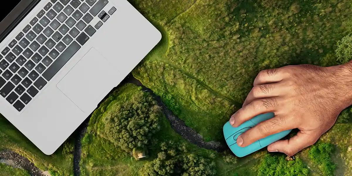 CRM na gestão de vendas de lotes: A imagem mostra uma mão humana com um dedo sobre um mouse de computador azul. O mouse está sobre uma paisagem verde, que parece ser uma representação de um mapa ou um plano de terra. Ao fundo, há uma parte de um laptop com o teclado visível, indicando que o mouse está sendo usado com o laptop. A combinação de tecnologia e natureza sugere uma conexão entre o mundo digital e o mundo físico.