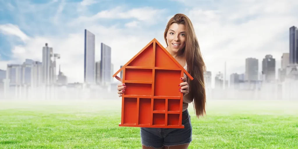 anúncios para lançamento imobiliário: A imagem mostra uma jovem sorridente segurando uma estrutura que parece ser uma casa em miniatura, de cor laranja. Ela está de pé em um ambiente ao ar livre, com um céu azul parcialmente nublado ao fundo. Ao fundo, há uma cena urbana com edifícios altos, sugerindo que a cena pode estar acontecendo em uma área perto de uma cidade. A jovem está vestida com calça curta e parece estar em um ambiente ao ar livre, possivelmente um parque ou uma área de lazer, com grama verde ao redor. A imagem tem um estilo de fotografia com um filtro que dá uma sensação de ilusão ou representação artística.