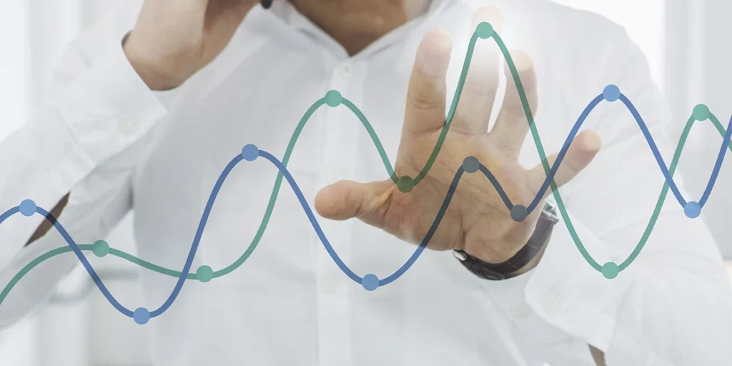 indicadores de inadimplência: A imagem mostra uma pessoa com um gesto de ponto ou indicação, com o braço estendido e o dedo ponteiro apontando para a direita. Ao fundo, há um gráfico de ondas azuis e verdes, que parecem representar dados de algum tipo de série temporal, como dados financeiros, de vendas, de tráfego de internet, ou outros dados que mudam ao longo do tempo. A pessoa está vestindo uma camisa branca e parece estar em um ambiente de escritório ou de trabalho.